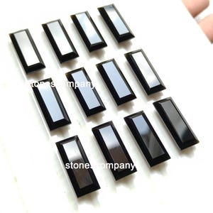 May include: A selection of rectangular black gemstones with a reflective, silver-coloured centre. The gemstones are arranged on a white surface. The text "stone company" is visible on some of the gemstones.