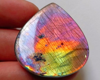 May include: A teardrop-shaped, polished gemstone with a vibrant display of colors. The stone features a mix of purple, pink, orange, and green hues, with a shimmering, iridescent effect. The surface has visible internal patterns.