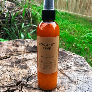 May include: A brown glass bottle with a clear spray nozzle. The bottle is labeled "Coconut Lime" and "Amber Street Soap Co.". The bottle is sitting on a tree stump.