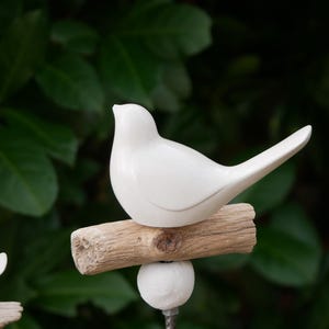 May include: White ceramic bird figurine perched on a piece of driftwood, attached to a metal rod with a white ball at the base. The bird is facing right and has a long tail.