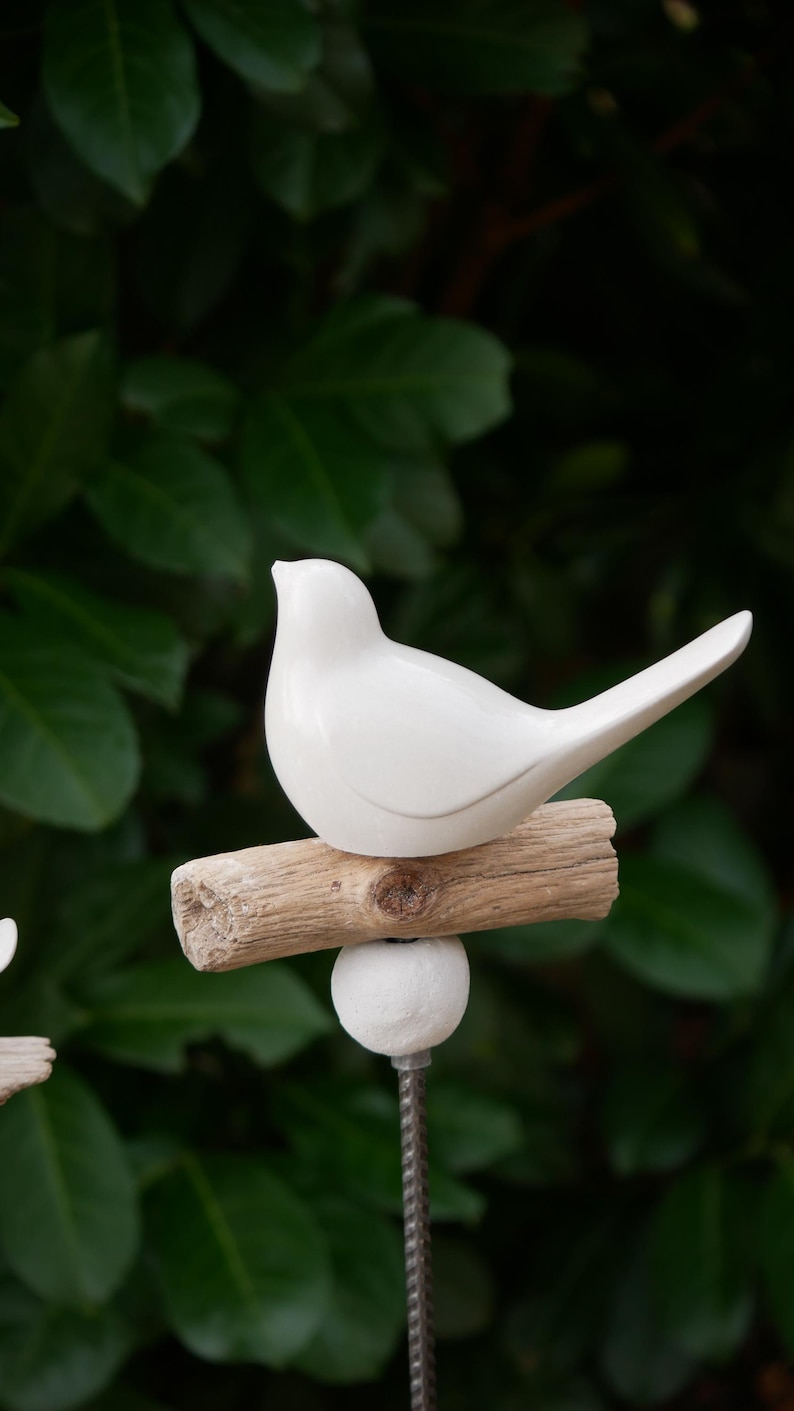 May include: White ceramic bird figurine perched on a piece of driftwood, attached to a metal rod with a white ball at the base. The bird is facing right and has a long tail.