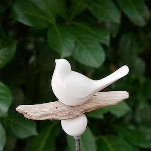 May include: A white ceramic bird perched on a piece of driftwood, attached to a metal stake with a white ceramic ball at the top.