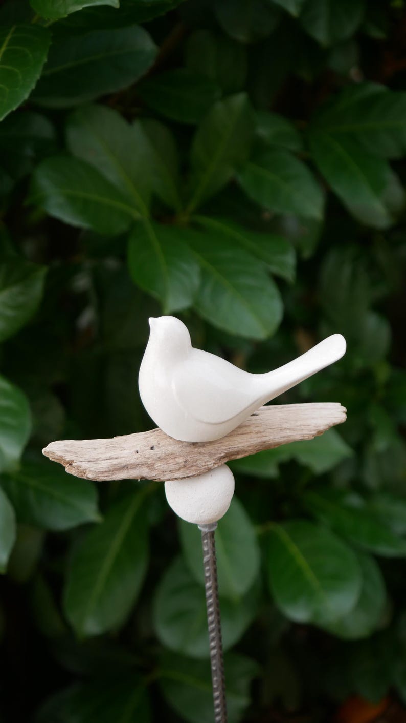 May include: A white ceramic bird perched on a piece of driftwood, attached to a metal stake with a white ceramic ball at the top.