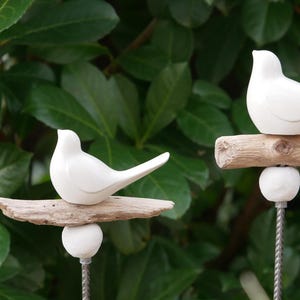 May include: Two white ceramic birds perched on driftwood branches. The branches are attached to metal stakes, creating a decorative garden stake set.