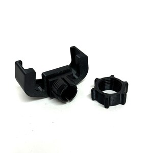 May include: Black 3D-printed plastic parts. One part is a U-shaped bracket with a threaded base. The other is a circular nut with a ridged exterior. Both parts are on a white background.