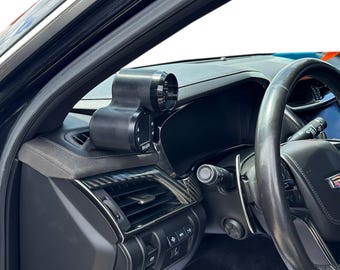 May include: Black automotive gauge pod mounted on a car's dashboard. The pod has a cylindrical gauge and a rectangular base. The dashboard is black with silver accents, and the steering wheel is visible on the right.