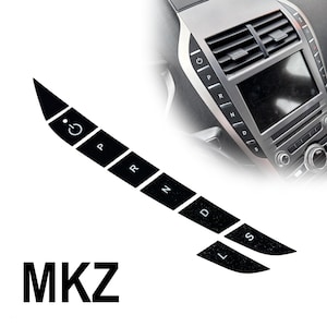 May include: A set of black adhesive gear shift button decals for a vehicle console, featuring white icons and letters including a power symbol, P, R, N, D, L, and S. The text MKZ is displayed below the decals, which are shown applied to a car interior.