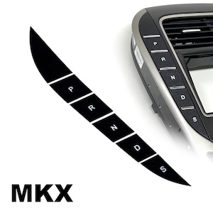May include: A black curved gear shift button panel for an MKX vehicle, featuring white P, R, N, D, and S labels. The panel is shown as a standalone strip and also installed on a dark gray automotive center console unit with air vents.