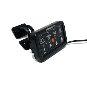 May include: A black control panel with the text "AUXBEAM" and various illuminated icons for lights and accessories. The panel includes buttons for fog lights, roof lights, and a fan. It has a mounting bracket and a black wire.