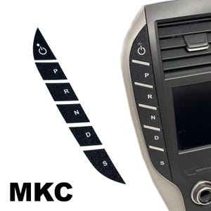 May include: A black, curved gear shift button decal strip featuring white icons for power, P, R, N, D, and S. The decal is shown both as a standalone strip and applied to the side of a vehicle center console dashboard panel labeled with MKC.