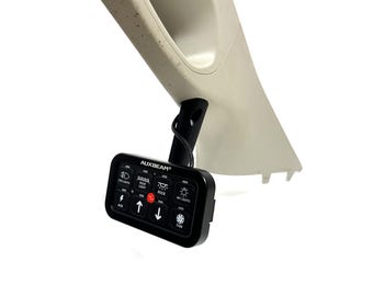 May include: A black control panel with the text "AUXBEAM" and various light and fan icons. The panel is mounted on a beige plastic car interior trim piece. The panel has buttons for fog lights, rock lights, and other functions.
