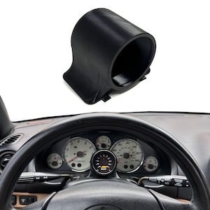 May include: A black cylindrical gauge pod mount designed for automotive dashboards. The mount features a hollow circular opening for a gauge and a contoured base. It is shown installed on a vehicle steering column, holding an AEM boost gauge.