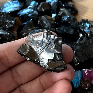 May include: A collection of black obsidian stones with iridescent rainbow hues. The stones are rough and have a variety of shapes and sizes.