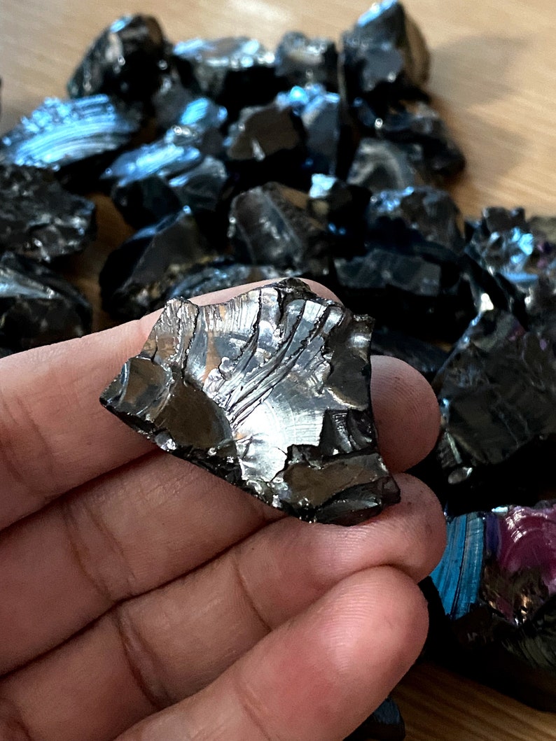 May include: A collection of black obsidian stones with iridescent rainbow hues. The stones are rough and have a variety of shapes and sizes.