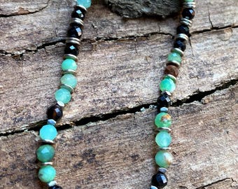 May include: A green and black beaded bracelet with a silver clasp. The bracelet is made with green gemstones, black onyx beads, and silver spacers.