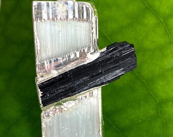 May include: Silver pendant featuring a black and white crystal design. The pendant is made of two rectangular pieces of crystal, one black and one white, set in a silver frame. The pendant is perfect for adding a touch of elegance to any outfit.