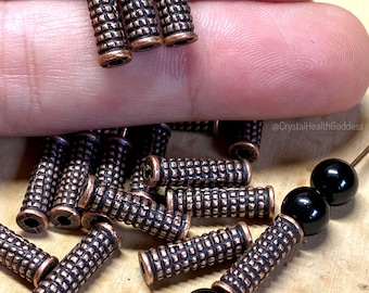 May include: A group of 20 copper-toned metal spacer beads with a textured design. The beads are approximately 1/2 inch long and 1/4 inch in diameter. The beads are shown with black round beads.