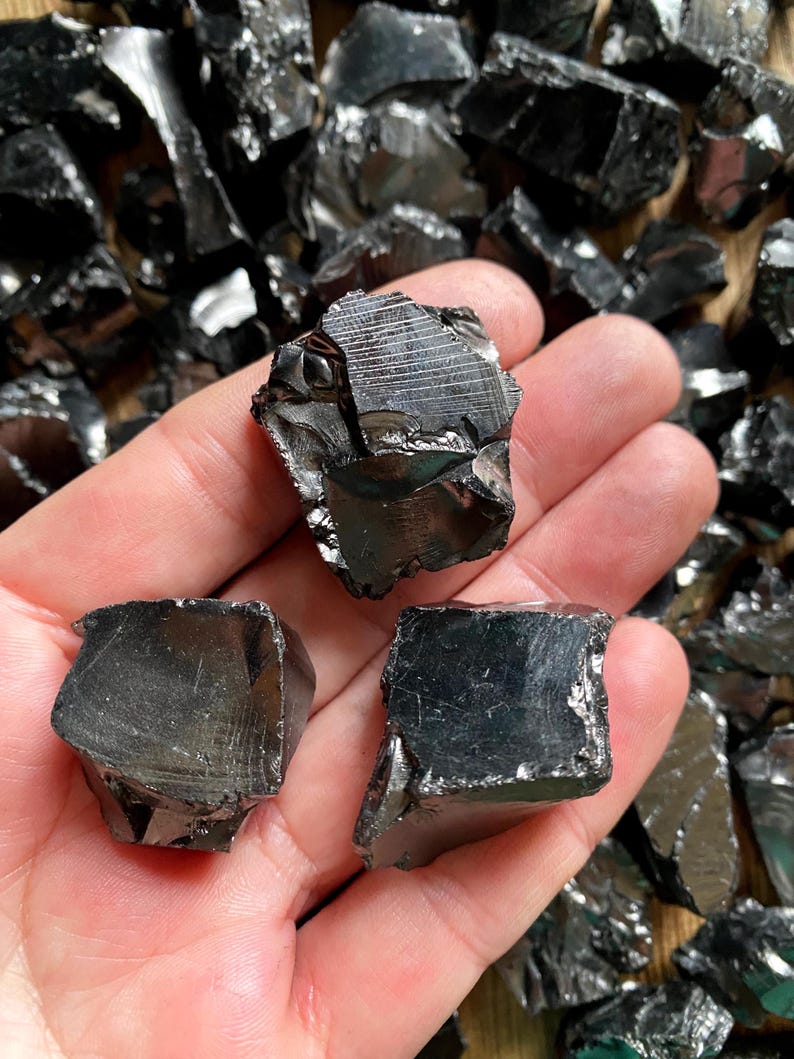 May include: A hand holding three pieces of black obsidian, a dark, glassy volcanic rock.