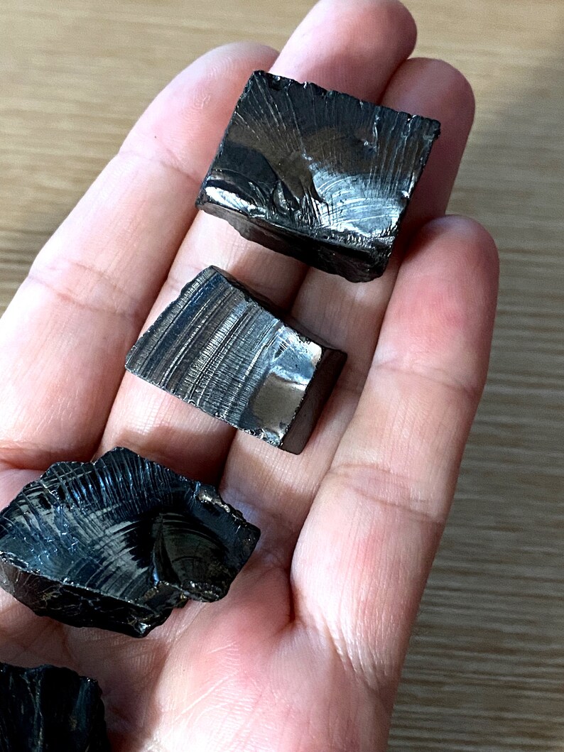 May include: Four black obsidian stones with a striated pattern. The stones are rough and have a natural, unpolished finish.