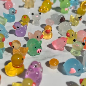 May include: A collection of colorful, translucent, miniature figurines of animals, including ducks, pigs, frogs, and an elephant. The figurines are made of a clear plastic material and have a variety of colors, including pink, purple, yellow, green, and blue.