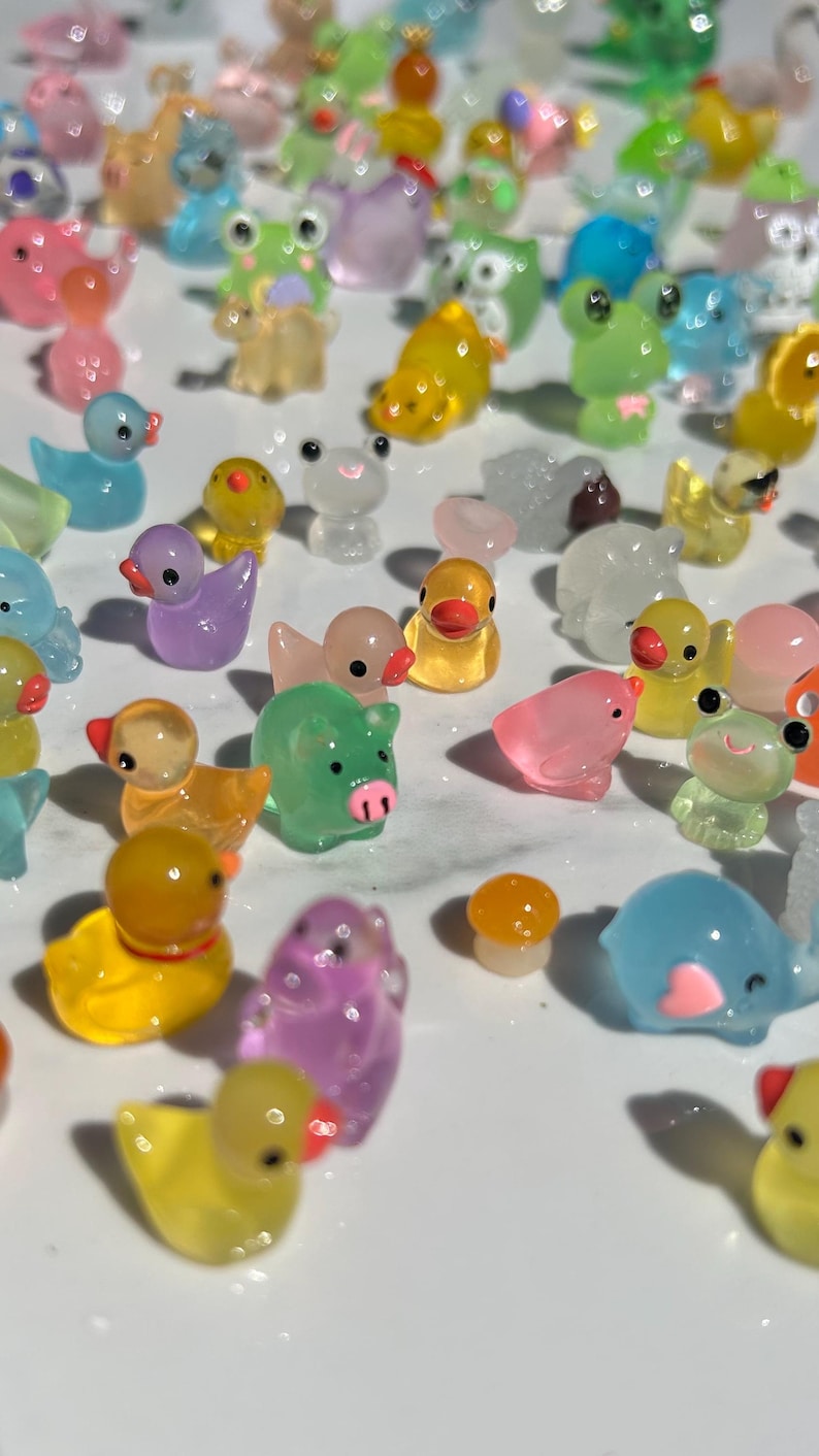 May include: A collection of colorful, translucent, miniature figurines of animals, including ducks, pigs, frogs, and an elephant. The figurines are made of a clear plastic material and have a variety of colors, including pink, purple, yellow, green, and blue.