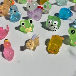 May include: A collection of colorful, small, clear plastic figurines of various animals, including a frog, a unicorn, a chick, a pig, an owl, a rabbit, a turtle, a chicken, and a dinosaur. The figurines are all about 1-2 inches tall and are made of a clear plastic with a slight shimmer.