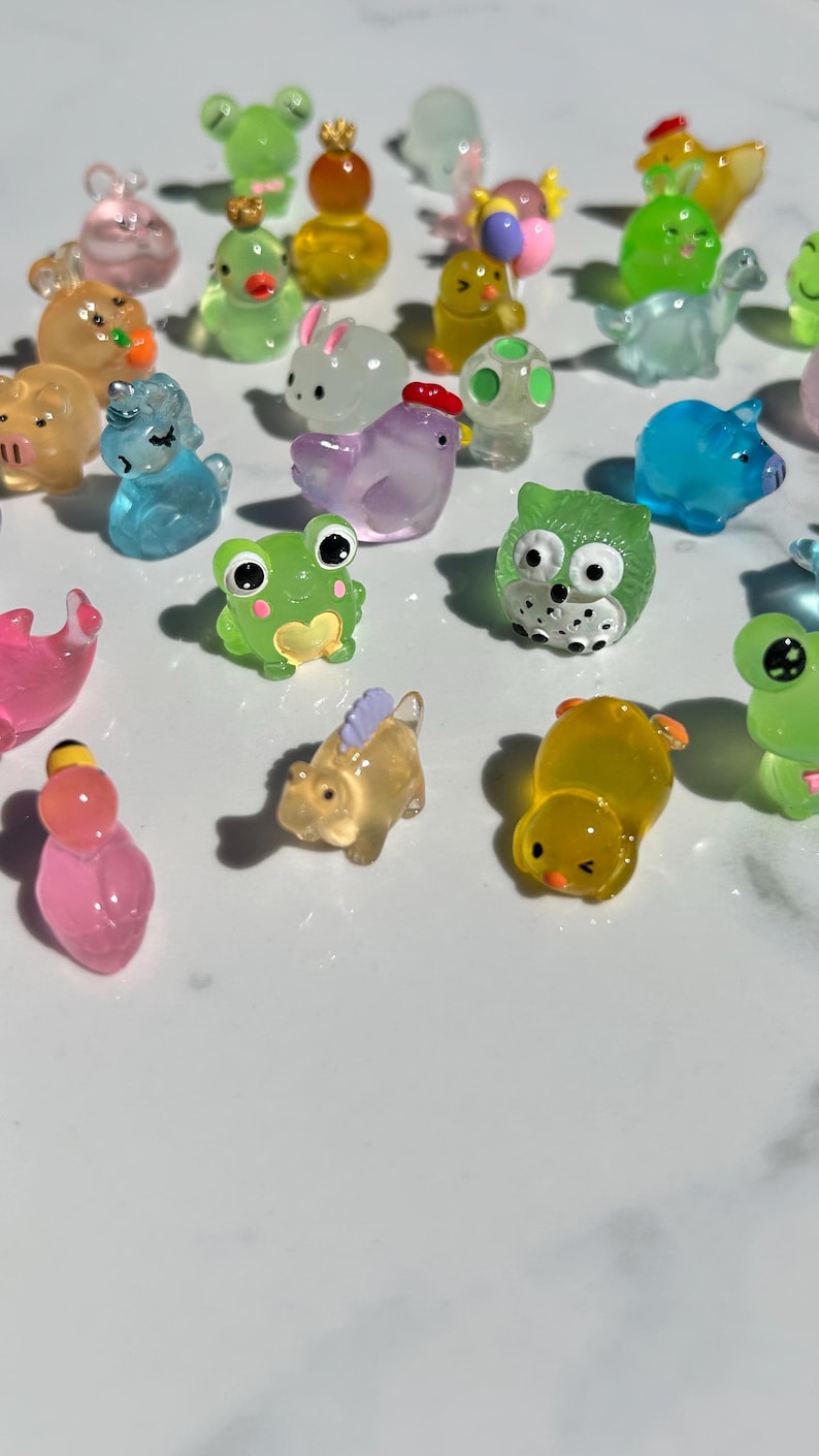 May include: A collection of colorful, small, clear plastic figurines of various animals, including a frog, a unicorn, a chick, a pig, an owl, a rabbit, a turtle, a chicken, and a dinosaur. The figurines are all about 1-2 inches tall and are made of a clear plastic with a slight shimmer.