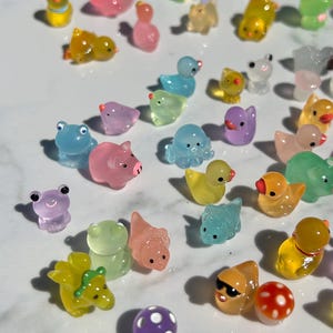 May include: A collection of colorful, translucent, miniature animal figurines. The figurines are made of a jelly-like material and feature a variety of animals, including a pig, a frog, a duck, an octopus, and a dinosaur.