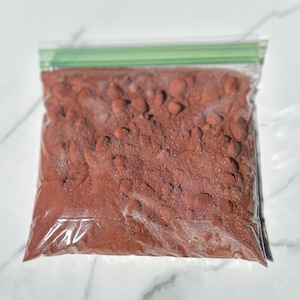May include: A clear plastic bag filled with a brown powder. The bag has a green zipper seal.