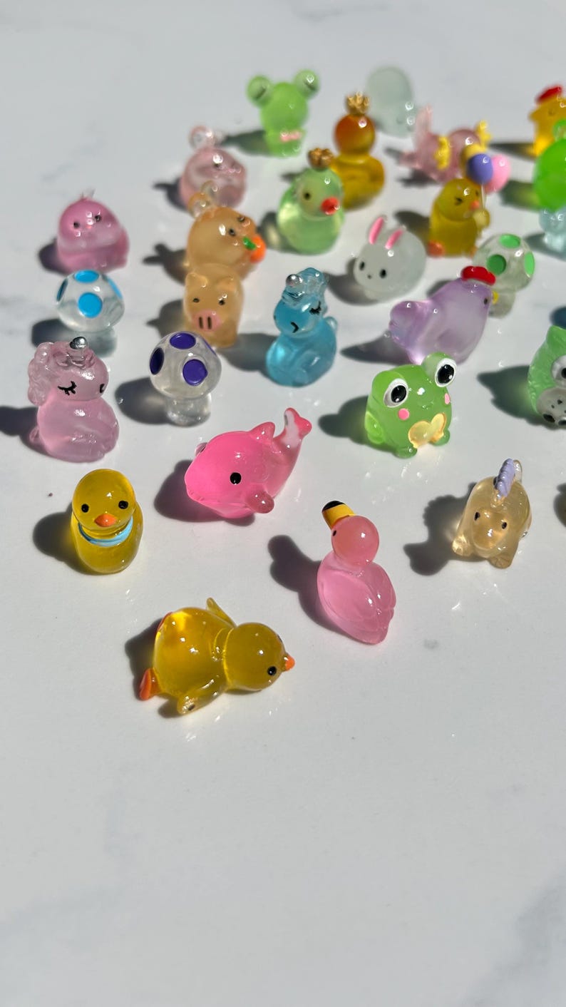 May include: A collection of colorful, translucent animal figurines. The figurines are made of a clear plastic material and feature various animal designs, including a duck, a dolphin, a frog, a unicorn, a bunny, and a mushroom.