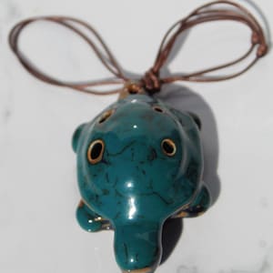 May include: A teal ceramic turtle ocarina with gold accents and brown cord necklace.