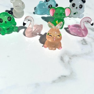 May include: A collection of small, clear plastic figurines of various animals, including a deer, panda, elephant, flamingo, rabbit, and frog. The figurines are all in different poses and have painted details.