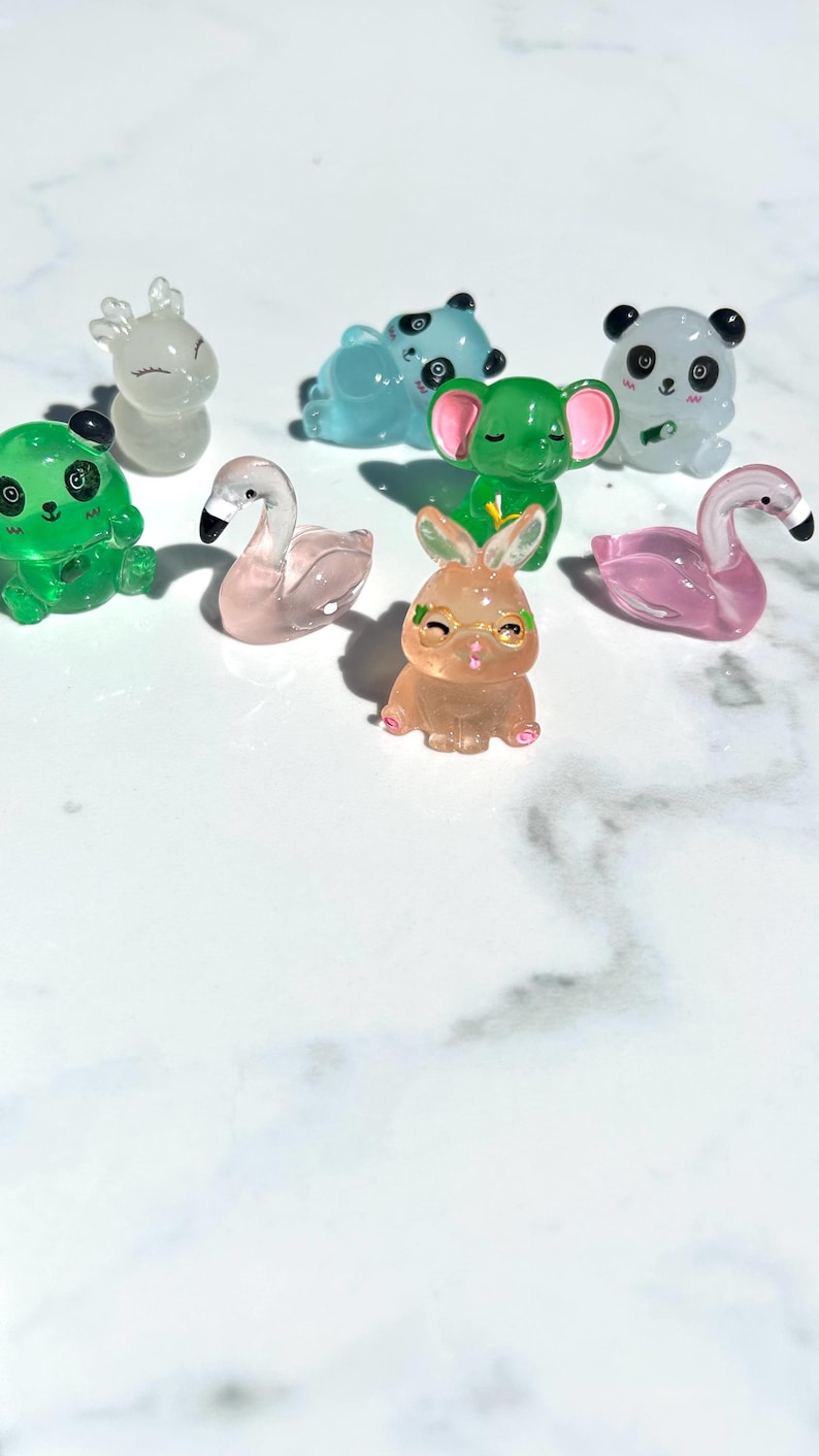 May include: A collection of small, clear plastic figurines of various animals, including a deer, panda, elephant, flamingo, rabbit, and frog. The figurines are all in different poses and have painted details.
