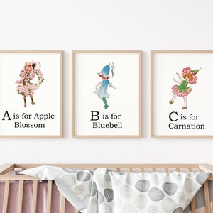 May include: Three framed prints with illustrations of children dressed as flowers. The first print features a girl with pink apple blossoms, the second print features a girl with a bluebell, and the third print features a girl with a carnation. The text below each image reads "A is for Apple Blossom", "B is for Bluebell", and "C is for Carnation".