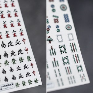 May include: Two sheets of white stickers with black, red, and green Chinese characters and symbols. The stickers are for a mahjong game.