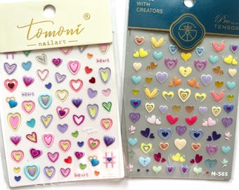 May include: Two sheets of nail art stickers with colorful heart designs. The stickers are on a white background and have the text "Tomoni nailart" and "heart" on them. The stickers are labeled "Pro Tensor" and "M-565".