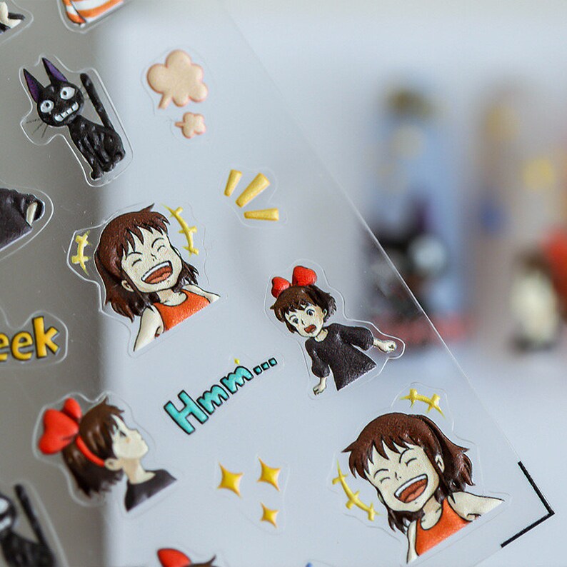 May include: A sheet of clear stickers featuring cartoon characters from the animated film 'Howl's Moving Castle'. The stickers include a black cat, a girl with red hair and a red bow, and a girl with brown hair and a red bow. The stickers also include text that says 'Hmm...' and 'eek'.