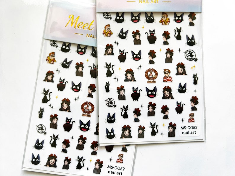 May include: Two sheets of nail art stickers featuring a black cat with a red bow, a girl with a red bow, and a boy with a red and white striped shirt. The stickers are on a white background with gold lettering that says "Meet Nail" and "Nail Art".