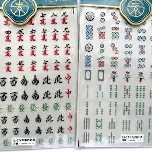 May include: Two sheets of mahjong tile stickers. The first sheet has red and black Chinese characters and the second sheet has green and black mahjong tiles. The text on the sheets reads "TS-274 Southeast Northwest Send" and "TS-275 Nine Cakes For".