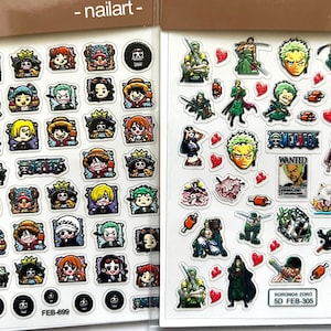 May include: Two sheets of nail art stickers featuring characters from the anime One Piece. The left sheet features a variety of characters, including Luffy, Zoro, and Nami. The right sheet features mostly Zoro, with some hearts and other designs. The text "WANTED" and "RORONOA ZORO" are visible on the sheets.