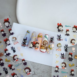 May include: A sheet of nail stickers featuring characters from the animated film 'Kiki's Delivery Service'. The stickers feature the main character Kiki, her black cat Jiji, and other characters from the film. The stickers are printed on clear sheets and are ready to be applied to nails.