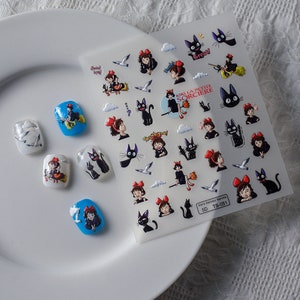May include: A sheet of nail art stickers featuring characters from the animated film Kiki's Delivery Service. The stickers feature Kiki, Jiji the cat, and other characters from the film. The stickers are printed on a clear sheet with a white background. The sheet also includes the text "Kiki La Petite Sorciere" and "Delivery Service".