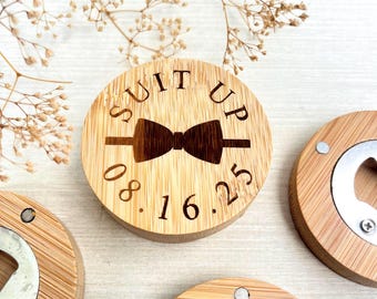 May include: Three round wooden bottle openers with a silver bottle opener mechanism. One bottle opener has the text "SUIT UP" with a bowtie and the date "08.16.25" engraved on it.