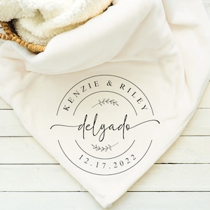 May include: A white throw blanket with a black circle design that says "Kenzie & Riley delgado 12.17.2022" with a small floral design above and below the text.