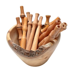May include: A wooden bowl filled with a collection of wooden dowels. The bowl is made of natural wood with a rough, bark-like texture. The dowels are all different lengths and have a smooth, polished finish.
