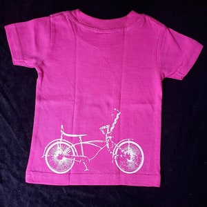 May include: A pink t-shirt with a white silhouette of a bicycle on the back.
