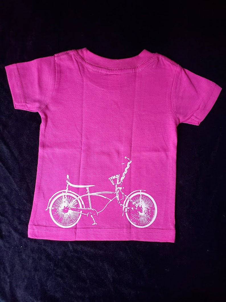 May include: A pink t-shirt with a white silhouette of a bicycle on the back.