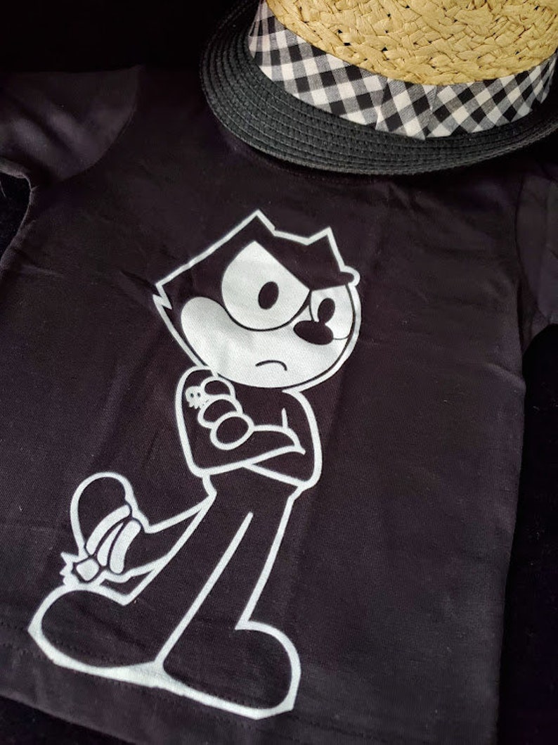 May include: Black t-shirt with a white graphic of a cartoon cat with a mischievous expression. The cat is wearing a white shirt and has a white outline.