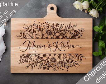 May include: A wooden cutting board with a floral design and the text "Mama's Kitchen" engraved on it. The board is light brown and has a handle on the top. The board is on a gray surface.