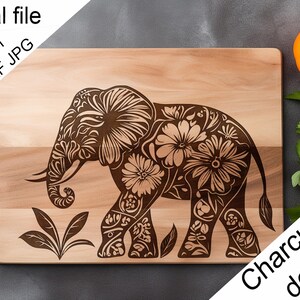 Peut inclure: Planche à charcuterie en bois avec un motif d'éléphant gravé. L'éléphant est orné de motifs floraux. La planche est rectangulaire et en bois clair. Une tomate et du persil sont en arrière-plan.